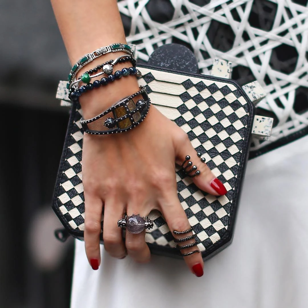 Jewelry, red nails, and a patterned clutch in a fashion detail photograph
