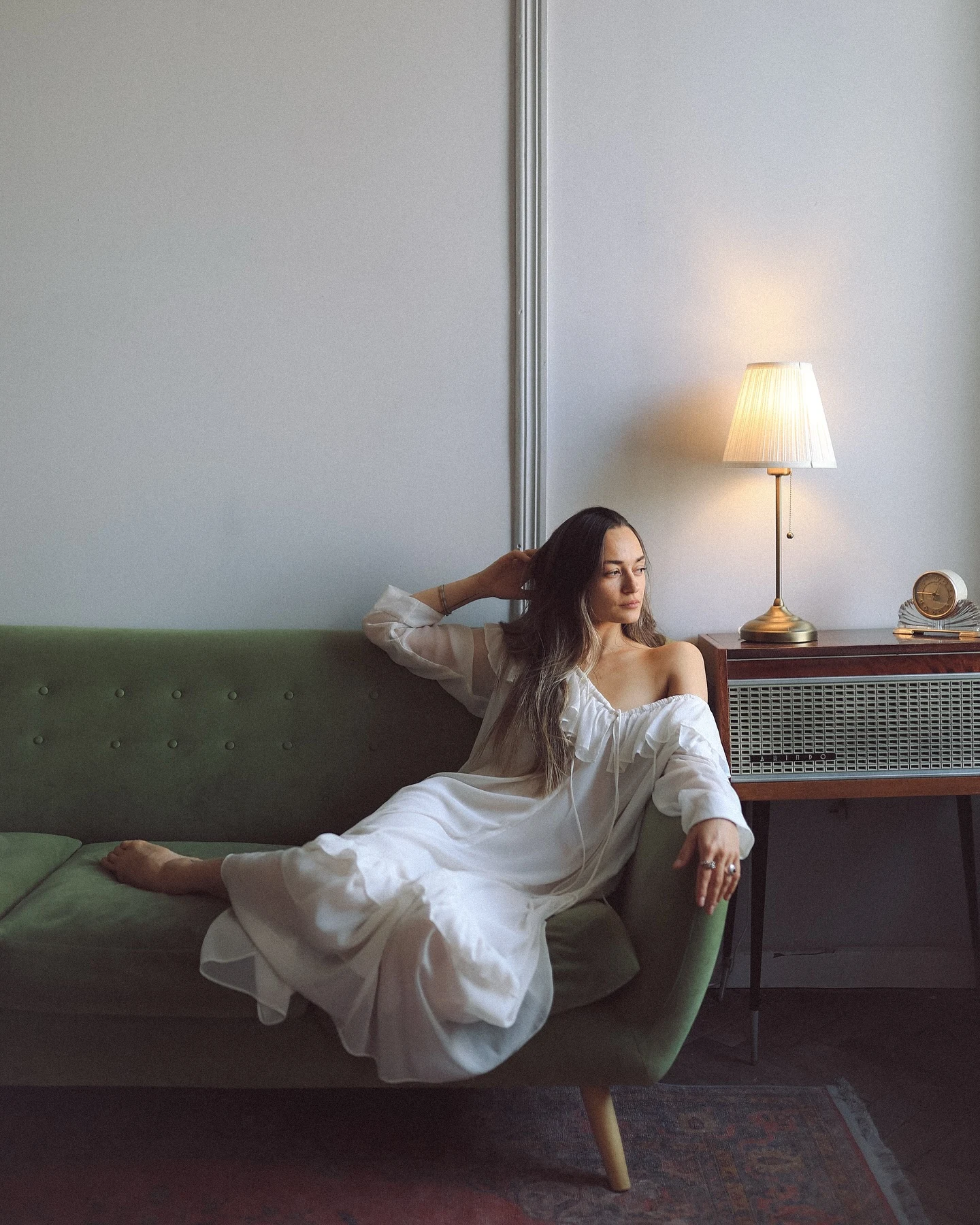 A woman in white seated on a green sofa beside a lamp